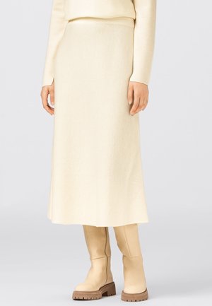 Kremfarvet strikket midi-nederdel med en glat tekstur, A-formet silhuet og høj talje. Kombineret med beige knæhøje støvler.