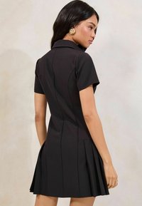 Black pleated dress with a collared neckline and short sleeves. Features rear seams and a textured finish for added detail.