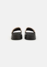 Sorte sandaler med strukturert såle og en flettet stoffrem langs den øvre kanten. Designet har en minimalistisk, åpen stil.