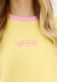 Żółta bluza z różową ściągaczem przy dekolcie i haftowanym logo "MÍRONS" w różowym kolorze. Miękka, gładka tkanina z okrągłym dekoltem.