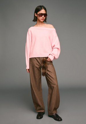 Lys lyserød off-shoulder sweater, brune breddebukser med en faux fur-detalje og mørkebrune slip-on sko. Solbriller fuldender looket.
