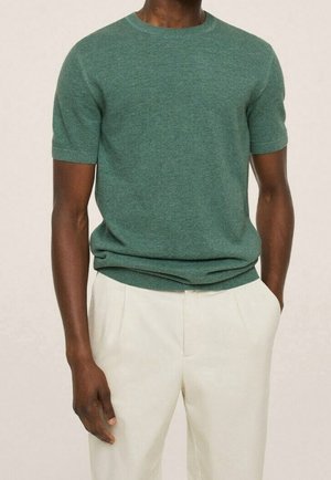 Zielony sweter z krótkim rękawem wykonany z teksturowanej dzianiny, z okrągłym dekoltem, lekko dopasowany krój, w połączeniu z jasnymi spodniami.