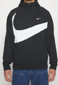 Svart huvtröja med vitt Nike-logotype och design detaljer. Har en halvdragkedja, långa ärmar och ribbade mudd. Tillverkad av mjukt tyg.