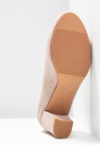 Chaussure pour femme en daim beige avec un petit talon carré, semelle en caoutchouc texturée, et étiquette de taille "37" visible sur la semelle.