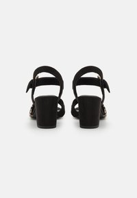 Sandales à talons hauts en suede noir avec des sangles de cheville ajustables et un talon bloc. Design à bout ouvert avec une texture lisse et un style minimaliste.
