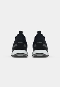 Black athletic sneakers with a textured upper, rubber sole, and a white midsole. Features "BOSS" branding on the heel and pull tabs.