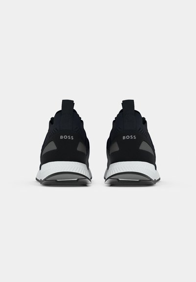 Baskets de sport noires avec une tige texturée, une semelle en caoutchouc et un entrecuisse blanc. Présente la marque "BOSS" sur le talon et les languettes.