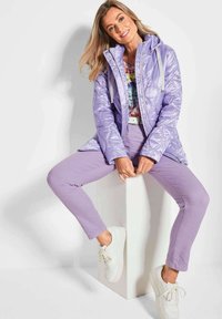 Lichtpaarse gewatteerde jas met een afneembare capuchon, gecombineerd met bijpassende lavendelkleurige broek en witte sneakers. De jas heeft drukknoopsluiting en zijzakken.