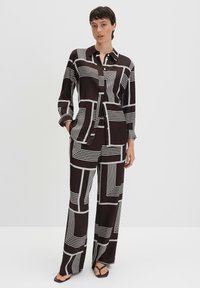 Zwart-wit gestreepte outfit gemaakt van gladde stof; heeft lange mouwen, een blouse met kraag en wijde broekspijpen met geometrische lijnen.