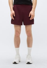 Μπορντό σορτς από ελαφρύ ύφασμα, με άνετη εφαρμογή και ελαστική μέση, συνδυασμένα με λευκές αθλητικές κάλτσες και παπούτσια.