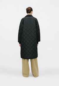 Pikowany czarny płaszcz o długim kroju, szerokich rękawach i kołnierzu. Charakteryzuje się lekko błyszczącą fakturą i wzorem w diamenty. Noszony na beżowe spodnie.