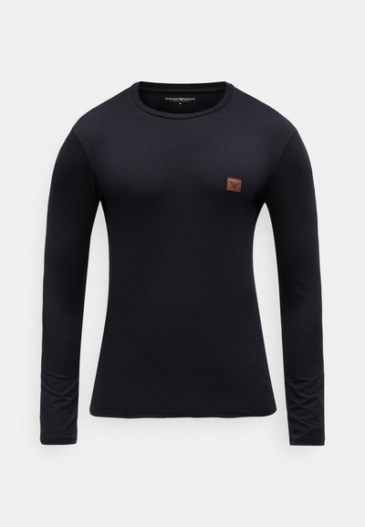 Melnas garām piedurknēm T-kreklam, izgatavotam no gluda auduma, ar apaļu izgriezumu un mazu brūnu logotipa uzlēkni augšējā kreisajā stūrī.