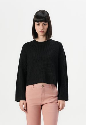 Black knitted cropped sweater with wide sleeves, textured fabric, round neckline, paired with pale pink fitted pants.