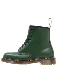 Zielona skórzana botka za kostkę z czarnymi akcentami, okrągłym noskiem, sześcioma oczkami, żółtym przeszyciem, trwałą podeszwą i pętlą do zakładania z tyłu.