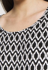 Haut à motifs noir et blanc avec un décolleté en forme de scoop, présentant un design texturé de formes allongées sur un fond uni.