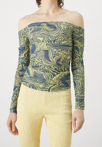 Off-the-shoulder top in blue and yellow swirl pattern, textured fabric with ruched sleeves, paired with yellow pleated pants.