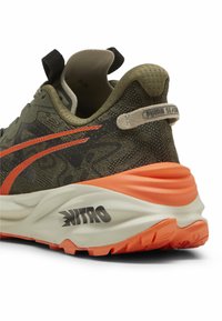 Sneaker z siateczkową górą w oliwkowym kolorze, pomarańczowymi akcentami i logo, wyściełaną białą podeszwą z fakturowanym gripem, z wzorzystym designem.