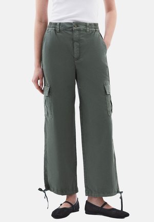 Groene cargobroek met een elastische tailleband, wijde pijpen, zijzakken en verstelbare zoomtouwen. Draagt met zwarte mesh flats.