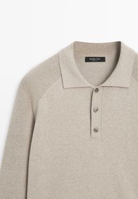 Polo color beige chiaro con colletto a coste, patta con tre bottoni e inserti testurizzati sulle maniche. Tessuto morbido, design casual.