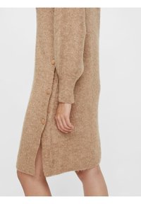 Úpletové šaty v světle hnědé barvě, s žebrovou texturou, bočním rozparkem a pěti kulatými knoflíky na levé straně.