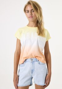 T-shirt met korte mouwen, met een verloop van lichtgeel naar oranje naar wit, met de tekst "PARADISE" in het wit gedrukt; gecombineerd met lichte denim shorts.