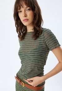 Top verde transparente con rayas texturizadas horizontales, mangas cortas y un diseño ajustado. Presenta un cinturón marrón con una hebilla dorada.