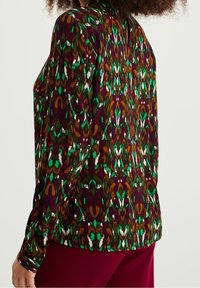 Blus med långa ärmar som har ett flerfärgat paisleymönster i grönt, bordeaux och brunt, tillverkad av mjukt, texturerat tyg.