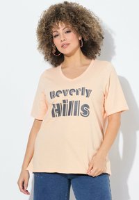 Meruňkové tričko s výstřihem do V a krátk�ými rukávy s černou grafikou "Beverly Hills", vyrobené z měkkého materiálu, s volným střihem.