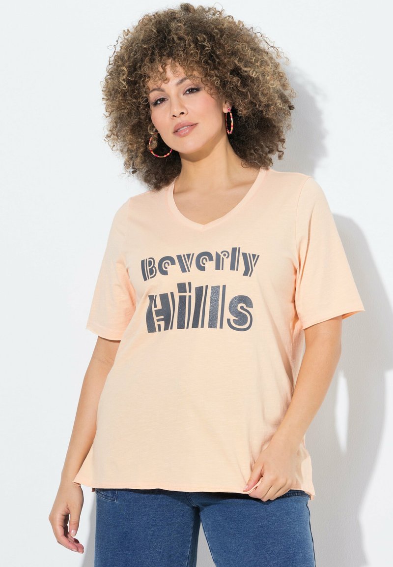 Meruňkové tričko s výstřihem do V a krátkými rukávy s černou grafikou "Beverly Hills", vyrobené z měkkého materiálu, s volným střihem.