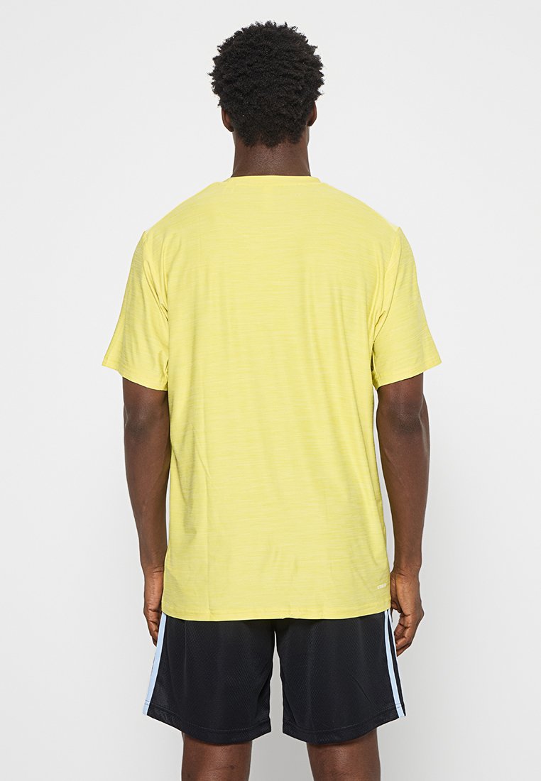T-shirt jaune à manches courtes en tissu léger et texturé, avec un col rond et une coupe décontractée, porté avec un short en maille noir.
