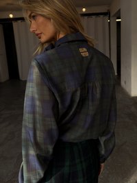 Sheer plaid shirt in dark green and navy, featuring a subtle gold hardware accent at the back. Long sleeves with loose fit.
