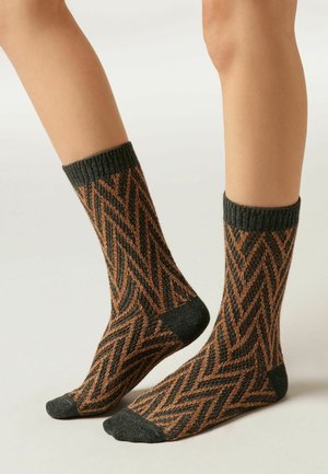 Chaussettes tricotées présentant un motif en zigzag orange et gris foncé, avec un poignet côtelé texturé. Le design est de longueur mi-mollet.