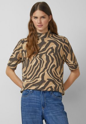 Beige Kurzarmoberteil mit hohem Kragen und schwarzem Zebra-Muster. Hergestellt aus einem weichen Material mit entspannter Passform. Tragen Sie es zu blauen Jeans.