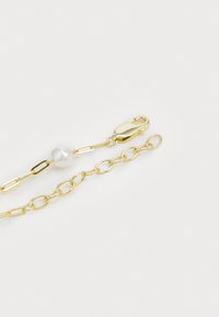 Bracelet en chaîne dorée avec des maillons allongés, une accent en perle et un fermoir robuste. Texture lisse et finition brillante.
