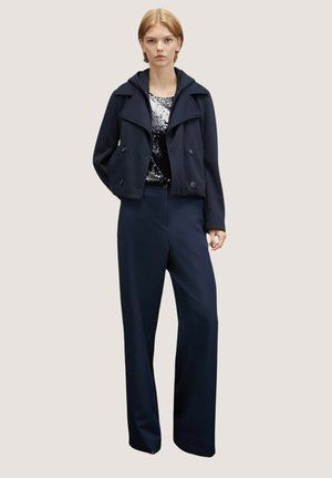 Chaqueta corta azul marino con capucha y botones de doble pecho, combinada con pantalones anchos azul marino y una blusa con lentejuelas debajo.