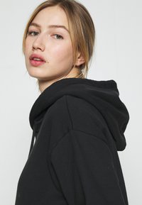 Felpa nera con cappuccio caratterizzata da una vestibilità rilassata, tessuto testurizzato e un cordino al cappuccio. Il design è semplice, senza loghi visibili.