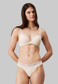 Beige polstret bh med tynne stropper og en glatt overflate, kombinert med matchende beige thong med en blondekantet midje.