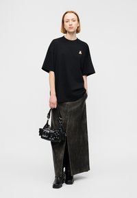 Μαύρο υπερμεγέθες T-shirt με μικρό έμβλημα αρκούδας, συνδυασμένο με μια μακριά, σκουρόκαφέ φούστα με εφέ δέρματος και μια μικρή μαύρη τσάντα χειρός με κεντήματα.