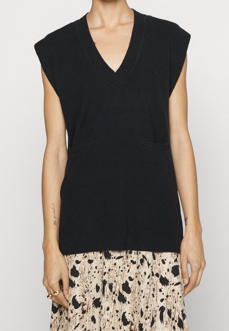 Svart V-ringad ärmlös topp med axelkappar, som har två framfickor och en mjuk textur, ihop med en mönstrad kjol.
