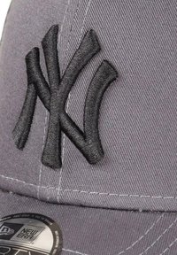 Gray cap made of fabric with an embroidered black NY logo. Features a curved visor and stitched detailing along the edges.