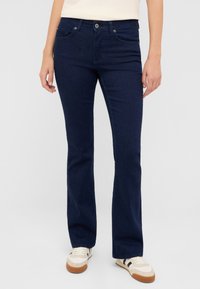 Granatowe dzwony z dżinsu, wyposażone w standardowe kieszenie, metalowe zapięcie na guzik oraz lekki połysk. Połączone z casualowymi sneakersami.