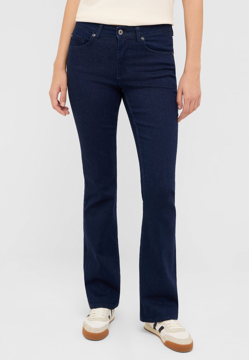 Granatowe dzwony z dżinsu, wyposażone w standardowe kieszenie, metalowe zapięcie na guzik oraz lekki połysk. Połączone z casualowymi sneakersami.