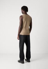 Top khaki fără mâneci, realizat dintr-un amestec de bumbac texturat, asortat cu pantaloni negri de tip loose-fit și pantofi negri. Design simplu, fără accente notabile.
