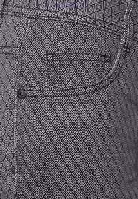 Zwart-wit gestreepte broek met een ruitpatroon, gestikte details en een zak met een zwarte knoopsluiting.