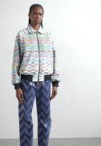 Une veste bomber matelassée colorée avec des bordures noires, associée à un pantalon marine à motif chevron en sequins.