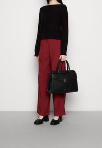 Svart läderhandväska med strukturerad form, ovandelshandtag och geometrisk klaff. Bärs med en svart tröja och bordeauxröda vida byxor.