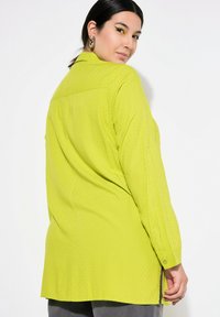 Limoengroene blouse met lange mouwen, met een knoopsluiting aan de achterkant, textiel met structuur en zijsplitten. Bevat een klassiek kraag en knopen bij de manchetten.