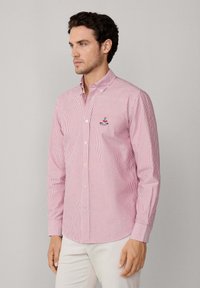 Camisa de botones a rayas rojas y blancas. Material de algodón con cuello tipo polo y logotipo bordado en el pecho. Mangas largas con puños de botón.