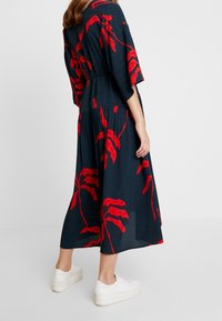 Námořnické květinové šaty s velkými červenými listovými vzory, krátké rukávy, elastický pas, splývavá sukně, v kombinaci s bílými teniskami. Texturovaná látka.