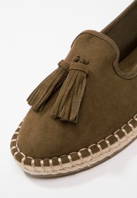 Braune Wildlederschlupfschuhe mit dekorativem Quast und gewebter Jutesohle mit kontrastierenden Nähten. Rund zulaufendes Design.